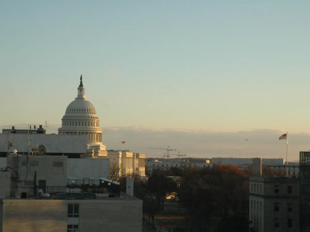 In this image there are buildings, trees, flags and sky. At the bottom of the image there is a...