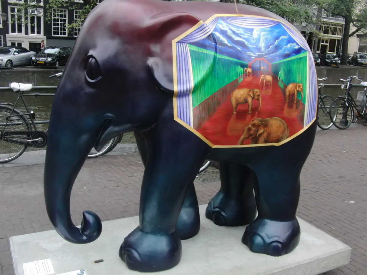 In this image there is an elephant statute, in the background there are bicycles, fencing, lake,...